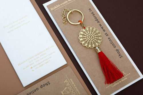 Floral design Rakhi for bhabhi with red hanging tassel cum keychain ring crafted in brass with golden finish